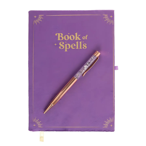 The Book of Spells Journal, a purple velvet hardcover notebook with gold detailing and a matching crystal-infused pen, perfect for journaling and spellcraft.