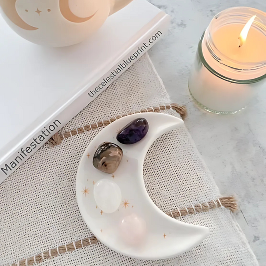 A crescent moon trinket dish with four healing crystals (Rose Quartz, Clear Quartz, Amethyst, and Rhodonite) arranged for manifestation, relaxation, and self-care. Styled with a lit candle, a manifestation journal, and a ceramic moon mug. A perfect addition to spiritual rituals, meditation, and mindfulness practices.