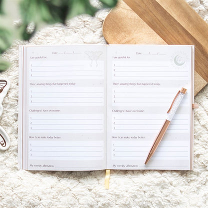 An open Luna Moth Daily Reflection Journal featuring gratitude prompts, affirmation sections, and space for daily reflections. Accompanied by a Clear Quartz Crystal Pen, this journal is designed for mindfulness, manifestation, and personal growth.